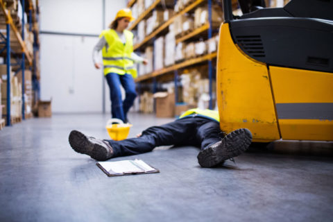 a man unconscious next to machine in warehouse and a coworker running to their aid