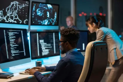 Cyber security specialist working at a computer station with coworkers in the background