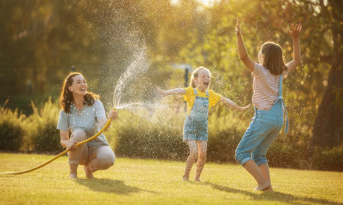 mom playing with her kids in the backyard, spraying them with a hose